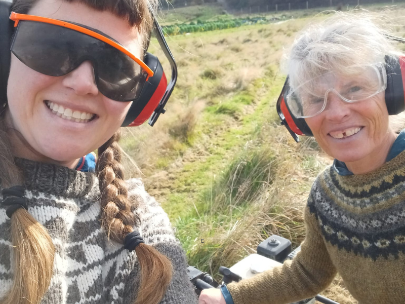 Two farmers in woolly jumpers wearing ear defenders while working in a field