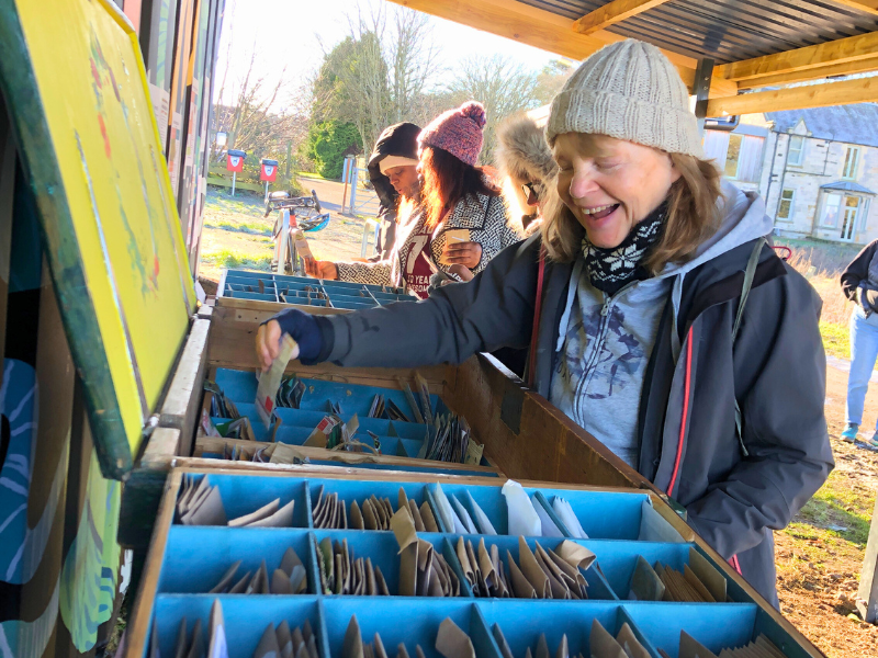 A delighted person picks out a packet of seeds from the Seed Kist, while others behind also browse and chat