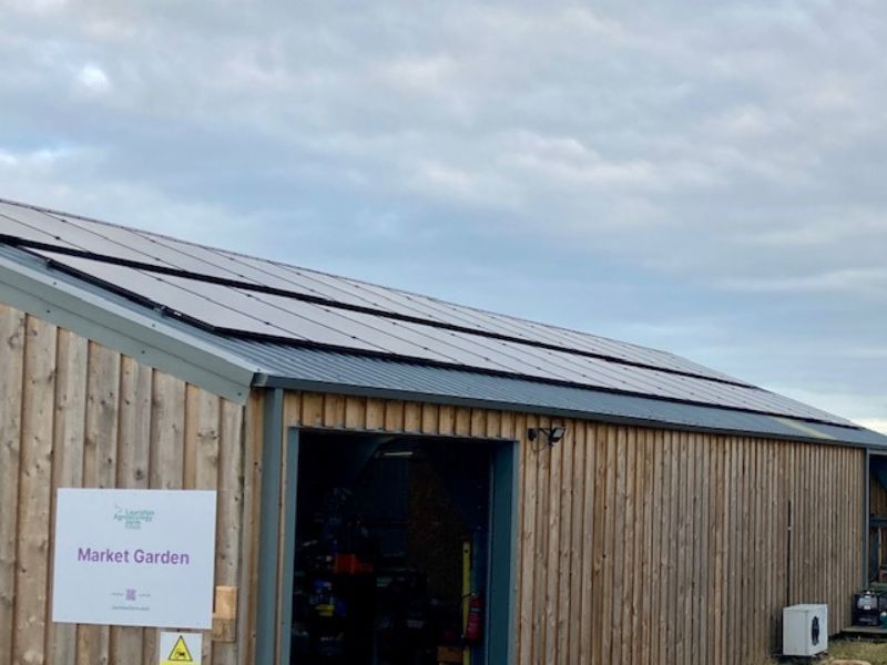 A photo of the pack shed with the sign 'market garden' at the end, and solar panels installed across the sloping roof