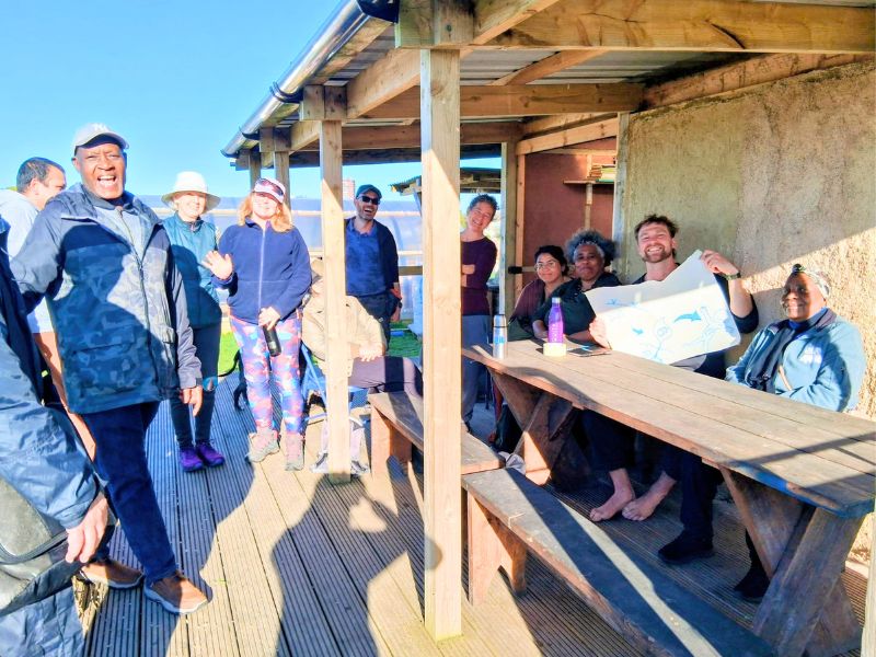 A group of smiling people gathered at the community kitchen, one holding up a large piece of paper with a diagram